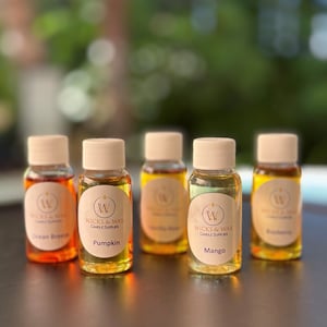 May include: Five small glass bottles with brown lids and labels. The labels are white with a gold logo and text. The bottles contain different colored liquids. The labels read "Ocean Breeze", "Pumpkin", "Vanilla Bean", "Mango", and "Eucalyptus".
