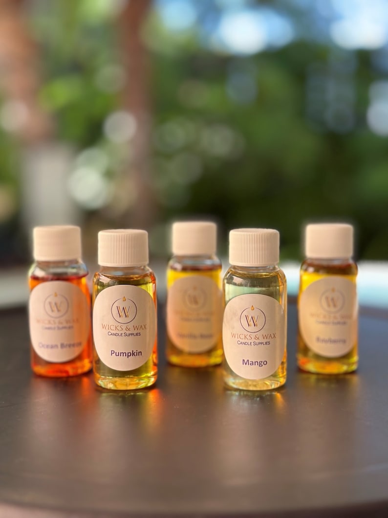 May include: Five small glass bottles with brown lids and labels. The labels are white with a gold logo and text. The bottles contain different colored liquids. The labels read "Ocean Breeze", "Pumpkin", "Vanilla Bean", "Mango", and "Eucalyptus".