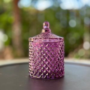 Könnte beinhalten: Ein violetter Glaskerzenbehälter mit Diamantenmuster. Der Behälter hat einen Deckel mit einem Knopf oben.