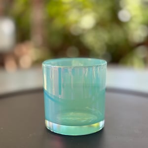 Puede incluir: Un vaso de vidrio azul claro con un diseño degradado blanco y azul. El vaso está sobre una superficie gris oscuro.
