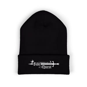 May include: A black knit beanie with a folded cuff featuring white embroidered text that reads Currently on a Side Quest. The design includes a small silhouette of a person on a horse and a sword graphic integrated into the lettering with stars.