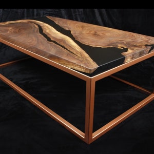 May include: A rectangular coffee table with a copper-colored metal frame. The tabletop is made of wood with a dark epoxy resin river running through the center. The wood has a natural grain pattern.