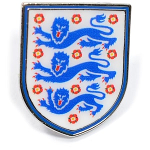 Puede incluir: Un pin de esmalte plateado y azul con el escudo de la selección nacional de fútbol de Inglaterra. El escudo representa tres leones azules sobre un fondo blanco con rosas rojas.