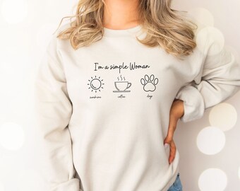 May include: A white sweatshirt with the text "I'm a simple woman" and three icons: a sun, a coffee cup, and a paw print. The icons are labeled "sunshine", "coffee", and "dogs".