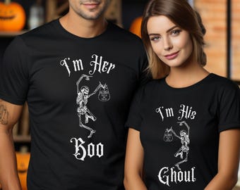 May include: Matching black t-shirts with white skeleton graphics and text for Halloween. One shirt says "I'm Her Boo" and the other says "I'm His Ghoul". The shirts are worn by a man and a woman, with carved pumpkins in the background.