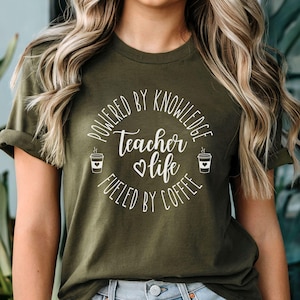 May include: A green t-shirt with the text "Powered by Knowledge Teacher Life Fueled by Coffee" in white lettering. The text is in a circle with two coffee cup icons on either side.