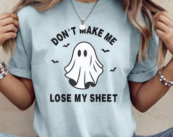May include: Light blue t-shirt with the phrase "DON'T MAKE ME LOSE MY SHEET" and a cartoon ghost illustration. The design includes small bat graphics. The shirt is a casual, unisex style.