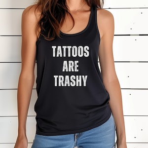 May include: Black tank top with the text "TATTOOS ARE TRASHY" in white block letters. The top has a racerback design and is made of a soft material. The tank top is worn by a person.