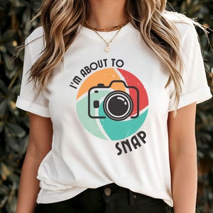 Op de afbeelding: Wit T-shirt met een retro-stijl camera-afbeelding en de tekst "I'm about to snap".