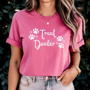May include: Pink t-shirt with white text that says "Treat Dealer" and paw prints with flowers.