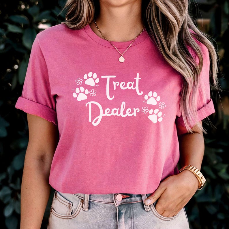May include: Pink t-shirt with white text that says "Treat Dealer" and paw prints with flowers.