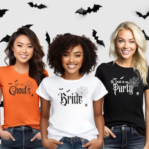 May include: Three women wearing Halloween-themed t-shirts. The shirts are orange, white, and black, each with a different spooky phrase in gothic font: "Let's Go Ghouls", "Bride", and "Till Death do us Party". Black bat cutouts decorate the background.