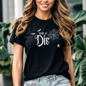 May include: Black t-shirt with the text "Bride or Die" in a gothic font, accompanied by bat and spiderweb graphics. The design is in white. A fun and spooky Halloween-themed tee.