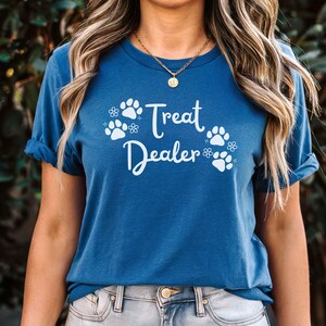 May include: A woman wearing a blue t-shirt with white paw prints and the text "Treat Dealer".
