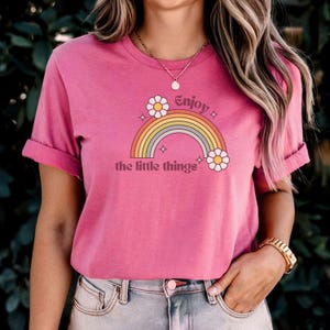 May include: Pink t-shirt with a rainbow and flowers graphic and the text "Enjoy the little things".