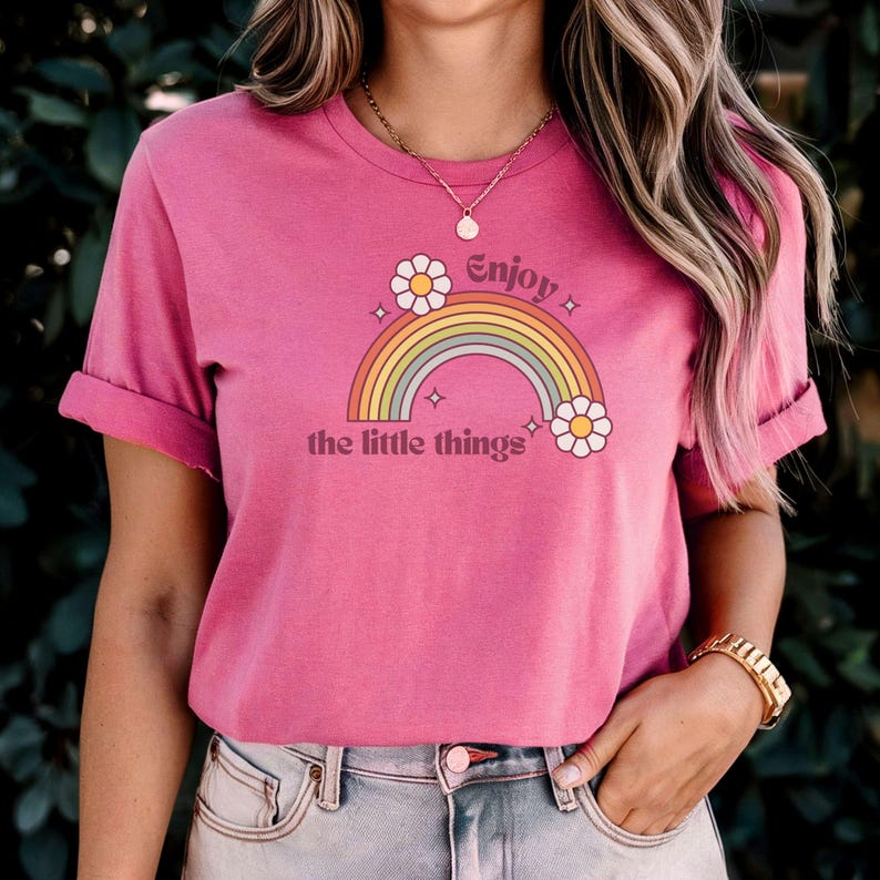 May include: Pink t-shirt with a rainbow and flowers graphic and the text "Enjoy the little things".