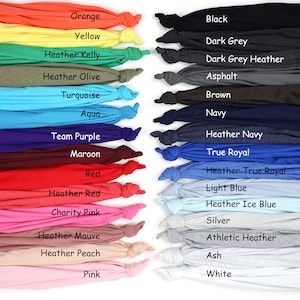 May include: A display of folded t-shirts in a range of colours, from vibrant orange and yellow to deep black and navy. Each shirt is labelled with its colour name, including "Orange" and "Black".