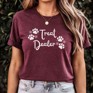 May include: A maroon t-shirt with white paw prints and the text "Treat Dealer" printed on the front.