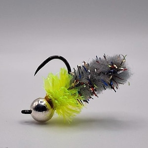 May include: A close-up of a fishing lure with a silver bead head, a black hook, and a gray body with colorful accents. The lure has a bright yellow, fluffy material near the hook.
