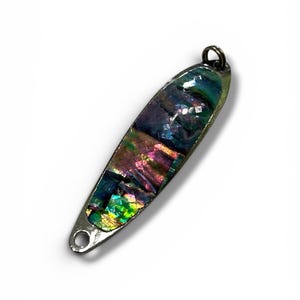 Pode incluir: Um pingente de metal de formato oval alongado com uma incrustação de concha de abalone iridescente e multicolorida. A superfície exibe tons variáveis de verde, roxo e rosa com um padrão texturizado de mosaico. Inclui um pequeno aro de metal.