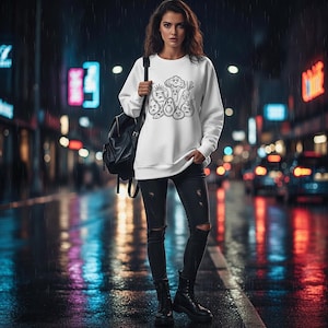 Puede incluir: Una sudadera blanca con una ilustración en blanco y negro de verduras antropomórficas. La persona lleva vaqueros negros rasgados y botas negras, con una mochila negra. El fondo es una calle de la ciudad por la noche.