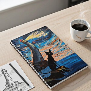 Puede incluir: Cuaderno de espiral con una colorida ilustración de un faro, un gato negro y un cielo dramático. Un lápiz y un boceto del faro están junto al cuaderno. Una taza de café blanca está cerca, con vapor saliendo de ella.