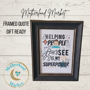 May include: A framed print with a black frame and gold trim. The print features a colorful graphic with the text "Helping People See is My Superpower".