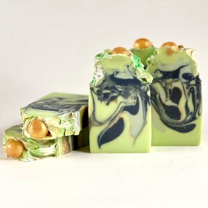 May include: Three bars of green and black marbled soap with gold flecks. The soap is topped with gold beads.