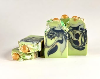 May include: Three bars of green and black marbled soap with gold flecks. The soap is topped with gold beads.