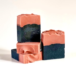 May include: Four bars of handmade soap, two are pink and black, and two are black and pink. The bars are stacked on top of each other.