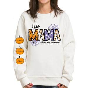 Pode incluir: Camisola branca com um gr&aacute;fico de "This Mama loves her pumpkins" em roxo e laranja com um design de teia de aranha e ab&oacute;bora. As mangas t&ecirc;m tr&ecirc;s ab&oacute;boras laranja com a palavra "Name" em cada uma.