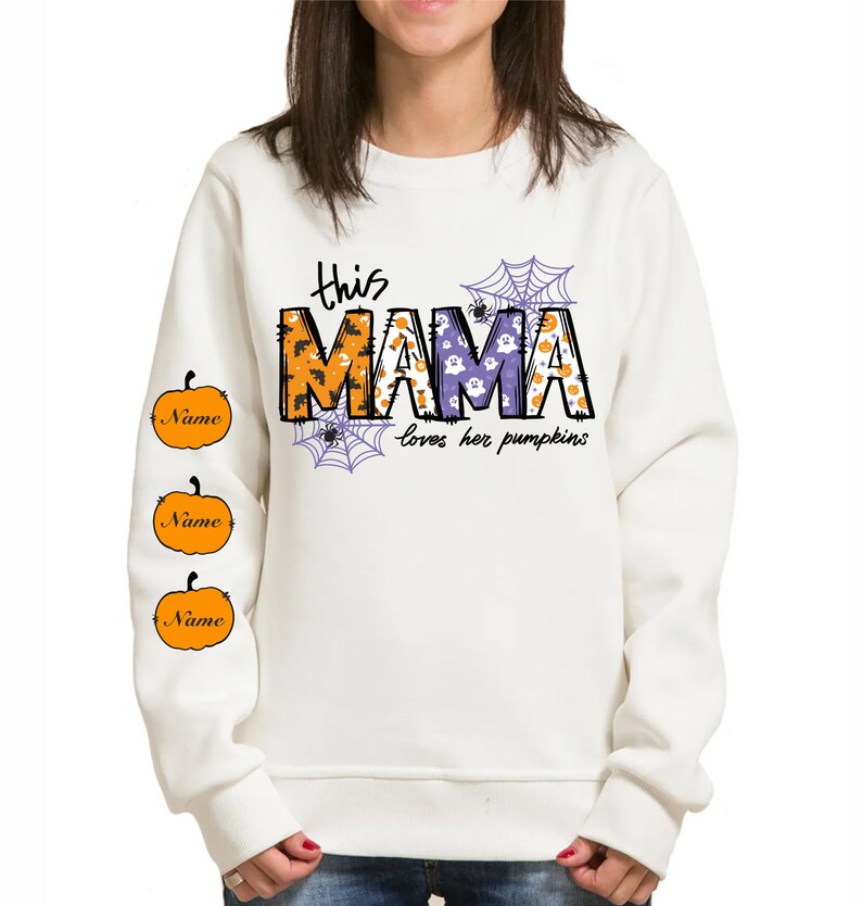 Pode incluir: Camisola branca com um gr&aacute;fico de "This Mama loves her pumpkins" em roxo e laranja com um design de teia de aranha e ab&oacute;bora. As mangas t&ecirc;m tr&ecirc;s ab&oacute;boras laranja com a palavra "Name" em cada uma.