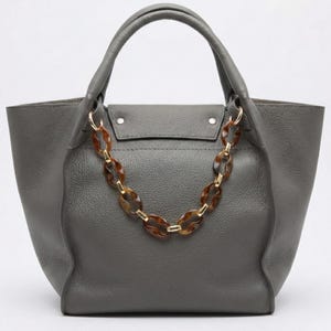 May include: A gray leather tote bag with a tortoiseshell chain handle. The bag has a structured shape with a top handle and a flap closure. The chain is made of oval-shaped links in shades of brown and gold.