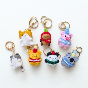 May include: A collection of handmade crochet keychains featuring various animal designs. The keychains include a cat, a capybara, a pig, a koala, a panda, and a bear, each with unique colors and details. They are attached to gold-colored key rings.