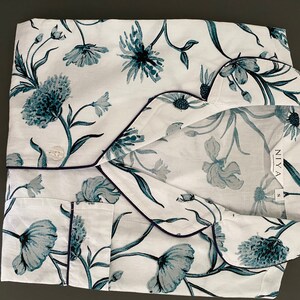 May include: White pajama top with a blue floral print and navy blue trim. The top has a button closure and a pocket on the left side. The brand name "NIYA" is printed on the tag.