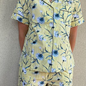 May include: A yellow and blue floral print pajama set with short sleeves and shorts. The set has a black trim around the collar, sleeves, and shorts.