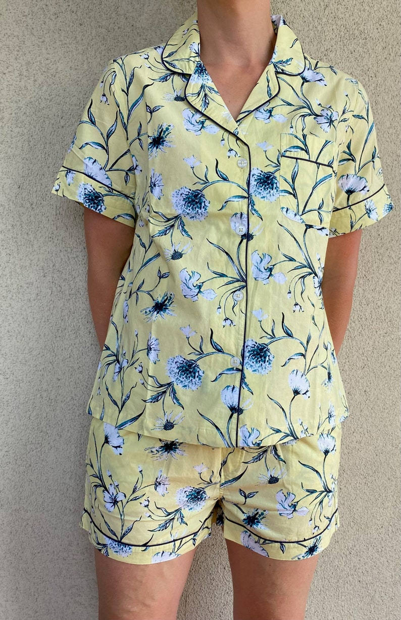 May include: A yellow and blue floral print pajama set with short sleeves and shorts. The set has a black trim around the collar, sleeves, and shorts.