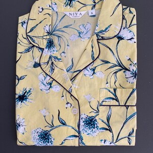May include: Yellow floral print pajama top with a black trim and a button closure. The top has a collar and a pocket on the left side. The brand name "NIYA" and size "S" are printed on the top.