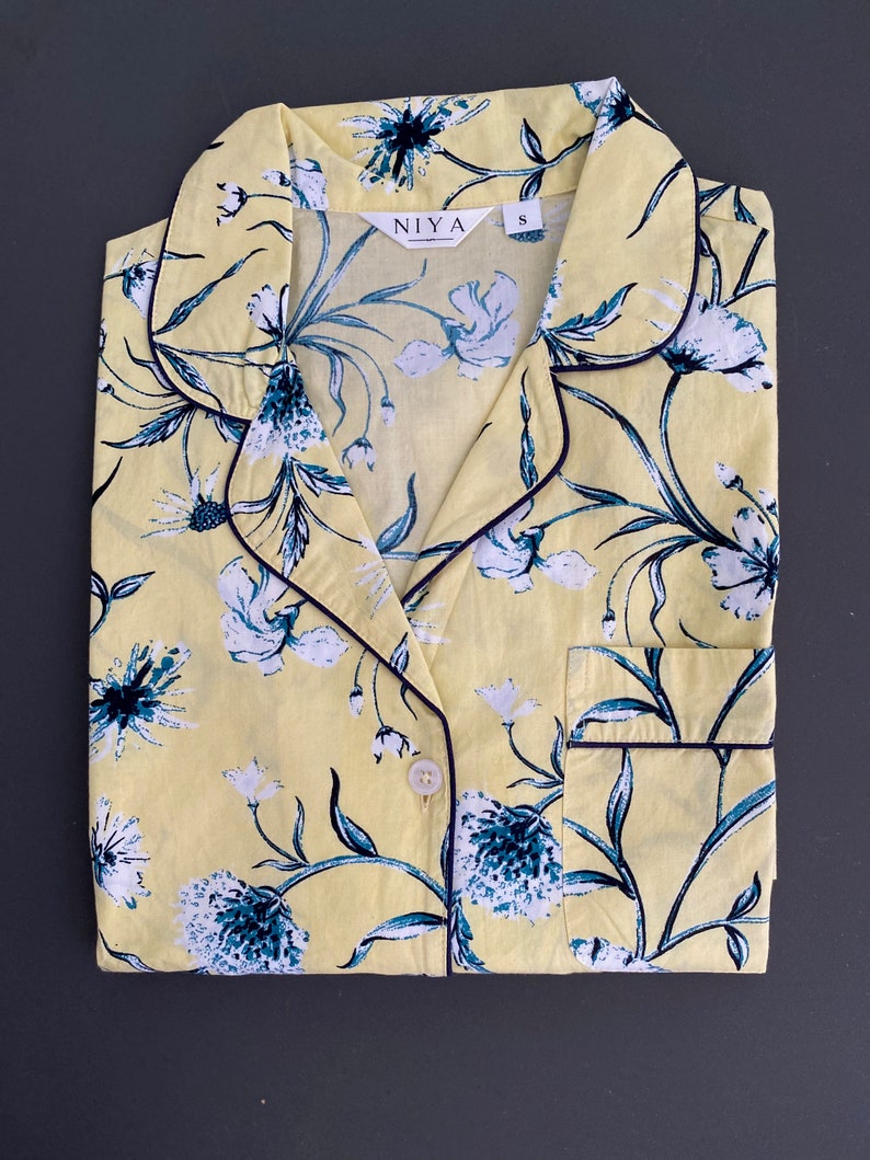 May include: Yellow floral print pajama top with a black trim and a button closure. The top has a collar and a pocket on the left side. The brand name "NIYA" and size "S" are printed on the top.