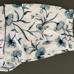 May include: White pajama shorts with a blue floral print. The shorts have a navy blue trim around the edges.