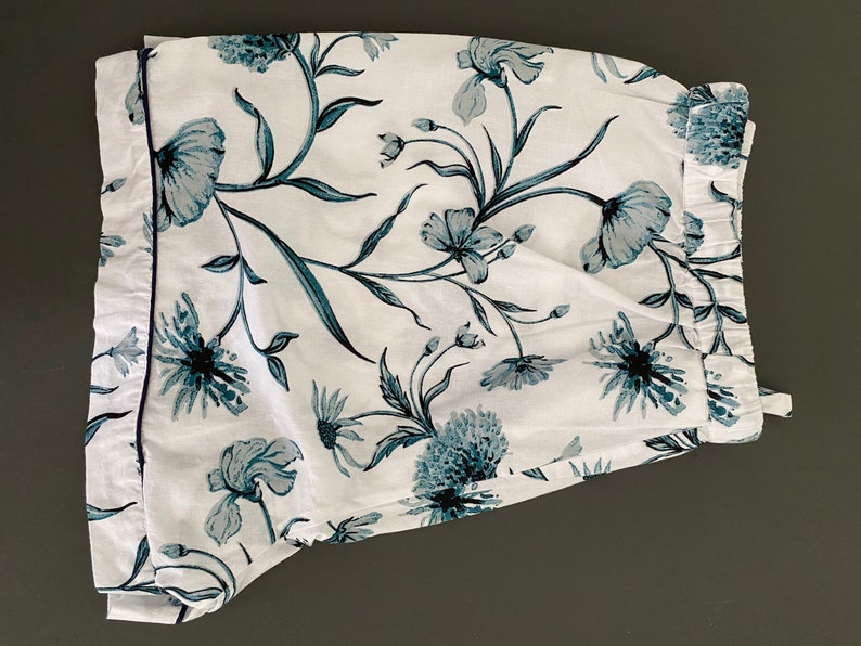 May include: White pajama shorts with a blue floral print. The shorts have a navy blue trim around the edges.