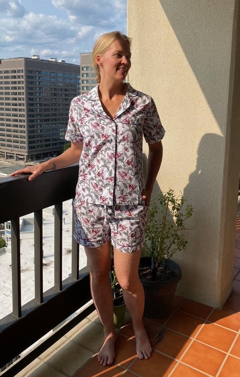 May include: A white and red floral print pajama set with short sleeves and shorts. The set has a collared shirt with a button-up front and a drawstring waist on the shorts.