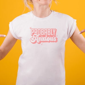 K&ouml;nnte beinhalten: Wei&szlig;es T-Shirt mit pinkfarbenem Text, der "PROBABLY Anxious" in einer Retro-Schriftart lautet.