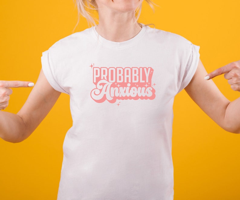 K&ouml;nnte beinhalten: Wei&szlig;es T-Shirt mit pinkfarbenem Text, der "PROBABLY Anxious" in einer Retro-Schriftart lautet.
