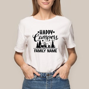 Puede incluir: Camiseta blanca con un dise&ntilde;o gr&aacute;fico negro que dice "Happy Campers" con una caravana y &aacute;rboles. El texto "FAMILY NAME" est&aacute; debajo del gr&aacute;fico.