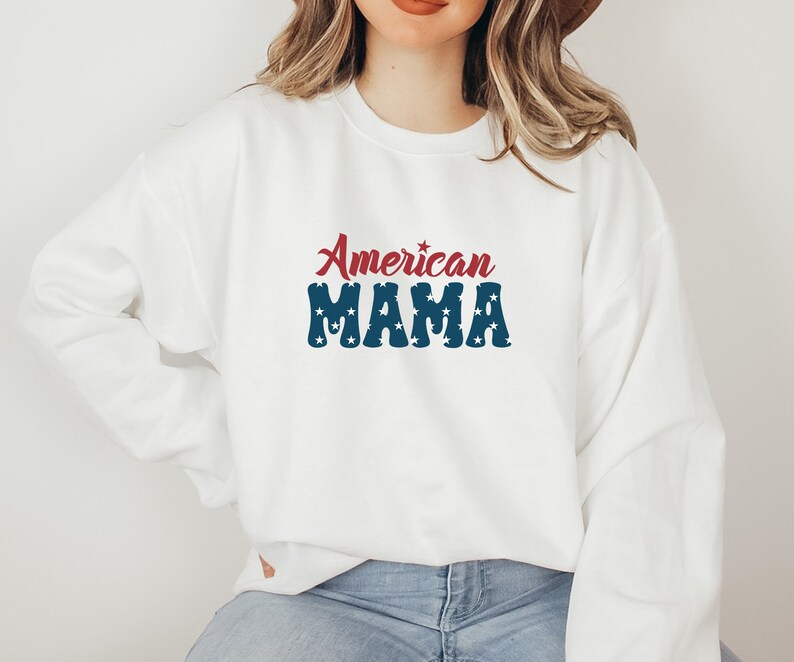 May include: White sweatshirt with the text "American MAMA" in red and blue. The word "American" is in a cursive font, and "MAMA" is in a block font with white stars. The sweatshirt is a casual style.