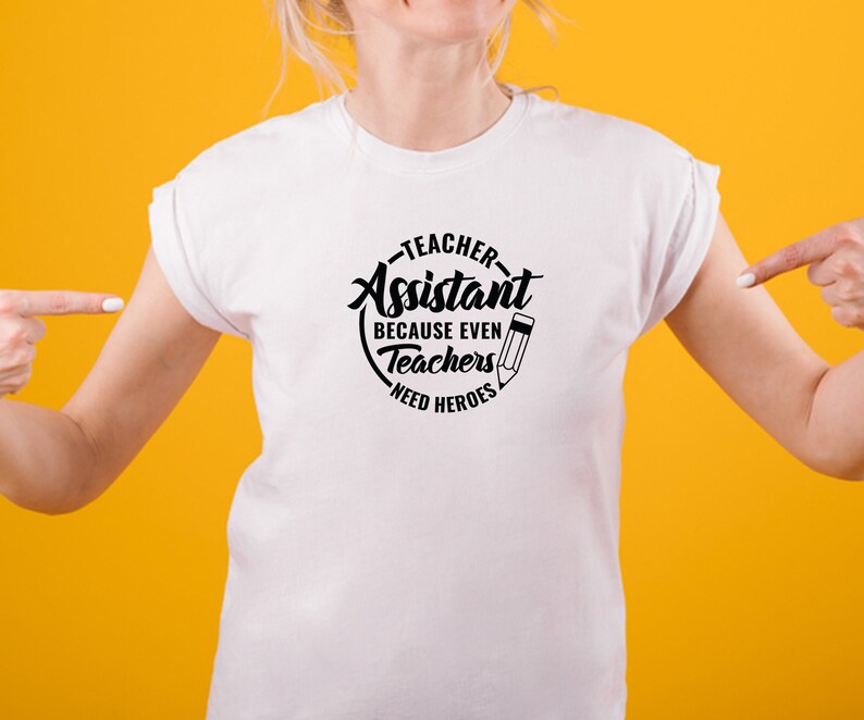 Pu&ograve; includere: Maglietta bianca con un grafico circolare nero che dice "Teacher Assistant Because Even Teachers Need Heroes" con un'icona di matita.