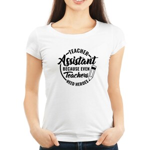 Pu&ograve; includere: Maglietta bianca con testo nero che recita "Teacher Assistant Because Even Teachers Need Heroes" con un'immagine di una matita.