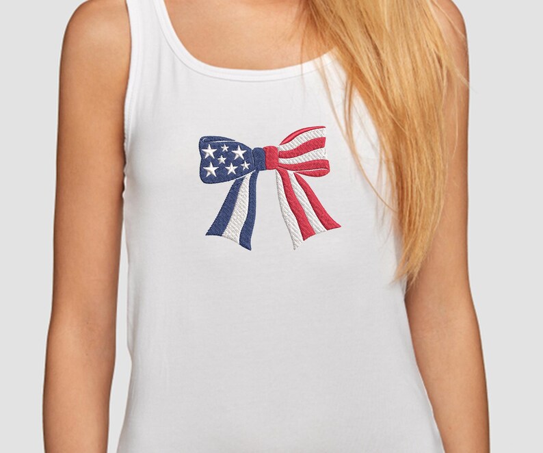May include: White tank top with an embroidered bow design. The bow features a patriotic color scheme with blue sections adorned with white stars, and red and white striped sections, evoking an American flag theme.