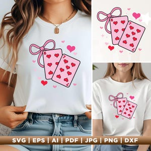 Puede incluir: Camiseta blanca con un lazo rosa y dos cartas de juego rosas decoradas con corazones rojos. Las cartas muestran el seis y el siete de corazones. Pequeños corazones rojos y un lazo rosa también en el diseño.